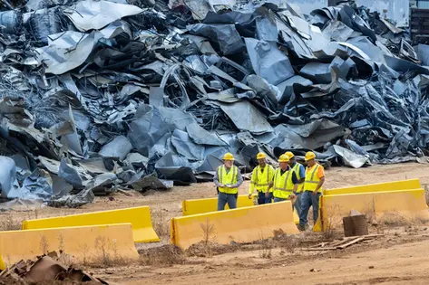 Group of construction workers inspecting a site near massive piles of scrap metal.