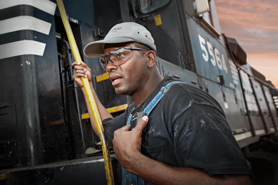 Rail worker in safety gear climbs engine steps at sunset for lifestyle product photography.