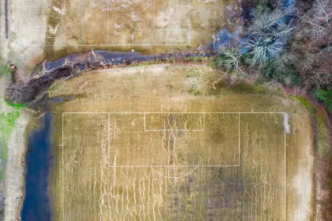 Aerial drone photography of a partially flooded soccer field bordered by trees and brush.
