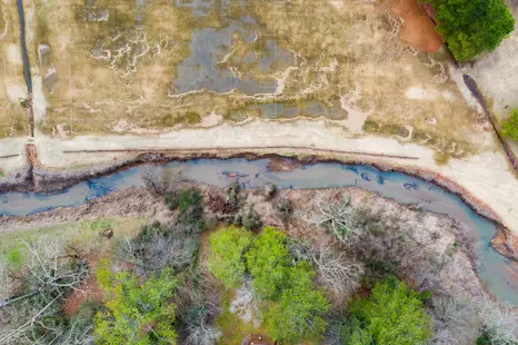 Aerial photography with drones showing a creek running between forest and soccer fields.