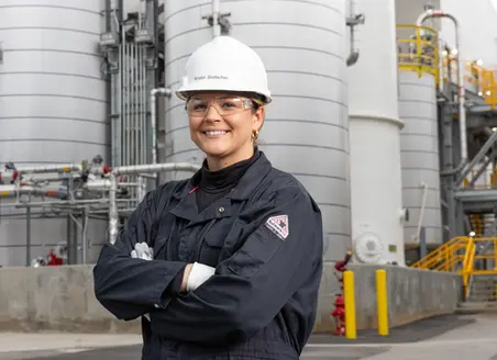 A business portrait of an industrial engineer in a hard hat and coveralls standing confidently at a processing plant.