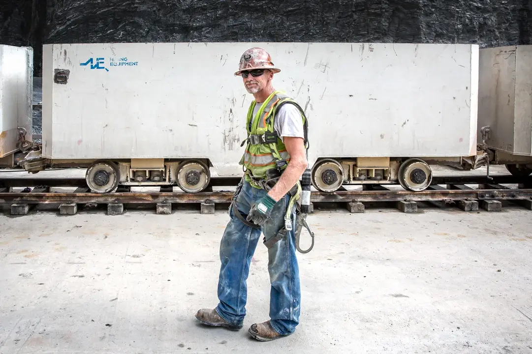 A business portrait of a miner in safety gear walking near mining equipment on a concrete yard.