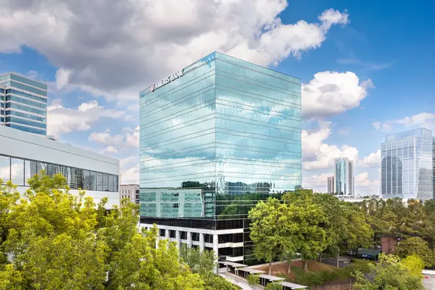 Aerial photography with drones capturing a mirrored office tower surrounded by trees and skyline.