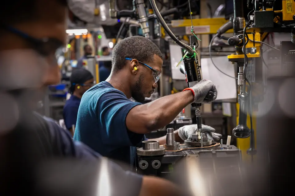Worker using a power tool or pneumatic device to assemble gears on a production line.
