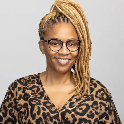 Corporate headshot photography of a woman with long blond locs, glasses, and a leopard print blouse, smiling confidently.