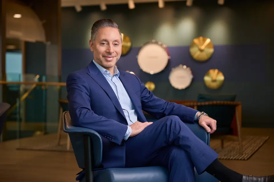 A professional business portrait of a relaxed executive seated comfortably in a contemporary office lounge.