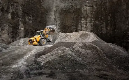 Yellow loader dumping gravel in a rocky quarry or mining site.