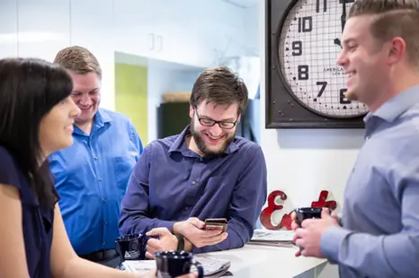 Coworkers chat over coffee in a modern office kitchen, reflecting casual connection in corporate lifestyle culture.