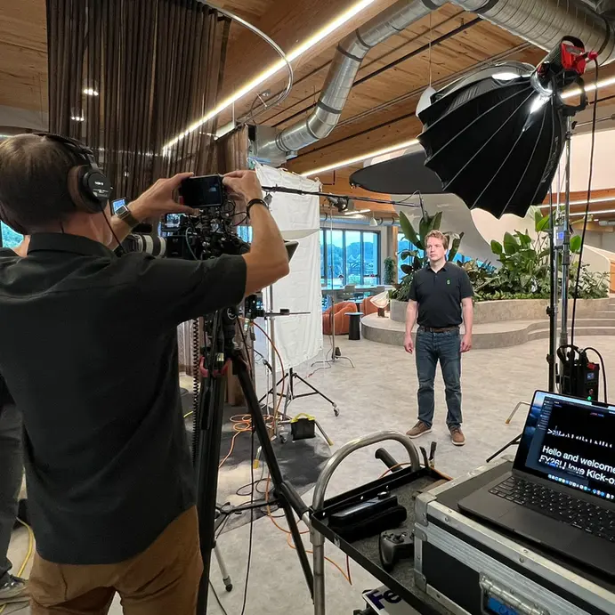 A camera crew films a man under studio lights in a modern office for a professional video shoot.