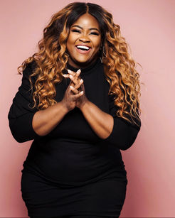 Melinda Watts, a christian mom influencer who is a plus size black woman with gorgeous long curly light brown hair, laughing brightly against a pink wall.