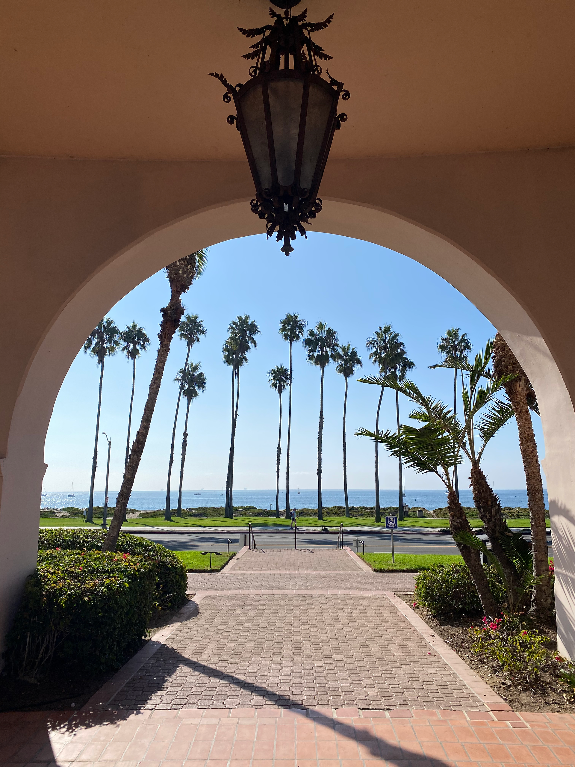 Spanish architecture with an arch revealing a path of palm trees lining the beach 