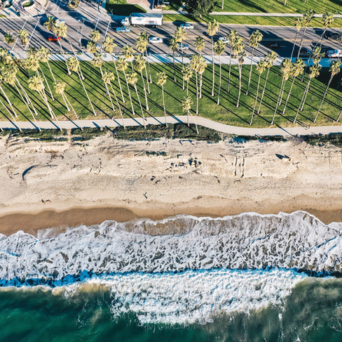 Aerial view looking down at the white sand beach with crashing waves and palm tree lines roadway with bike path at Hilton Santa Barabara