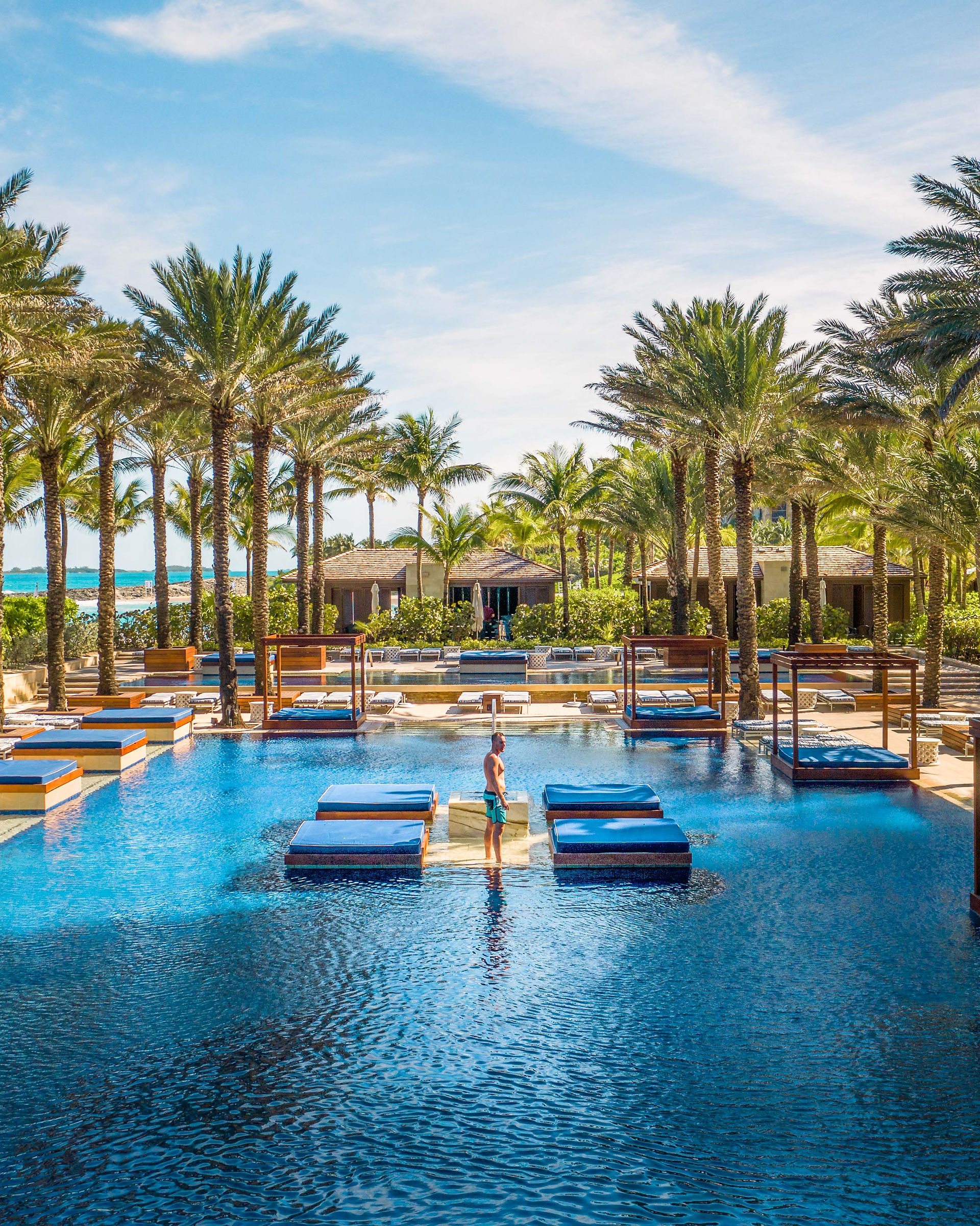 man standing in a day bed island in the middle of the pool surrounded by cabanas and palm trees at the cove Atlantis 