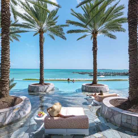 woman in sun hat lounging in a day bed at the infinity pool that overlooks the blue ocean waters 