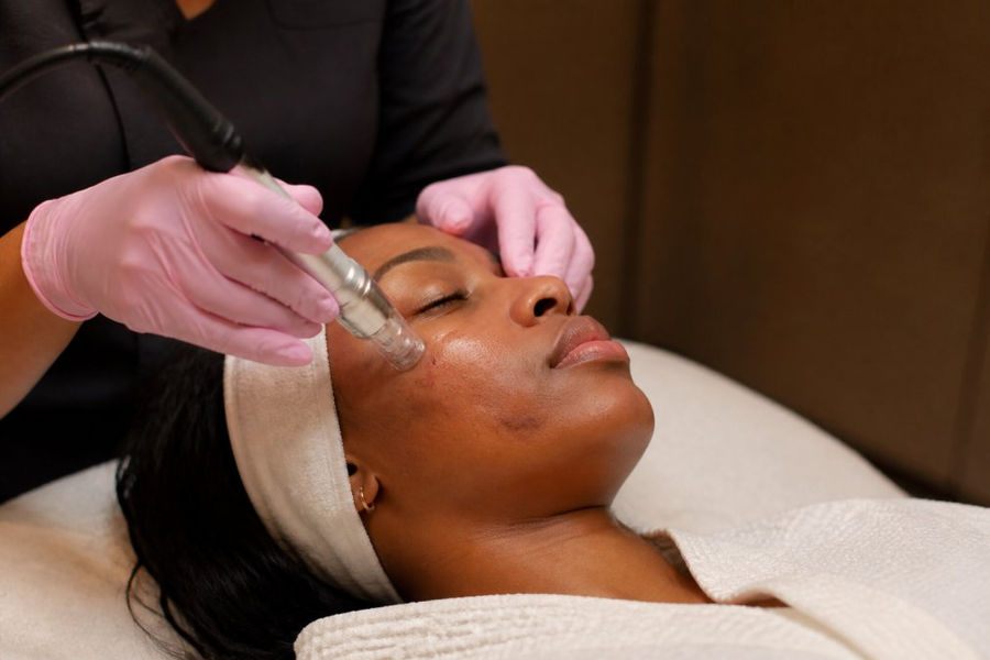 Person with melanated skin receiving professional aesthetic treatment in a clinical setting with warm lighting and professional care environment, showing the treatment area and clinical aesthetic equipment