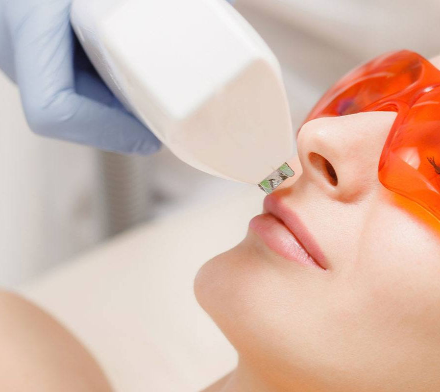 Mujer recibiendo tratamiento láser facial con gafas protectoras en un centro de estética.