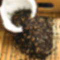 Coconut shell overflowing with Rooibos | Mandarin Chai, spilling onto wooden tray.