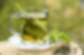 Glass cup with tea and green leaves on a wooden surface.
