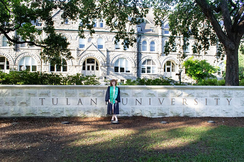 graduation photo of a woman in front of the Tulane University sign in New Orleans