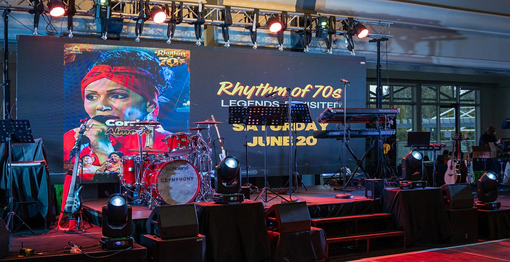 A wide shot of  a stage setup, with PA systems and Stage lighting and a Big Screen