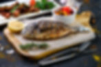 grilled fish on oiled paper and wooden cutting board surrounded by grilled tomatoes, grill