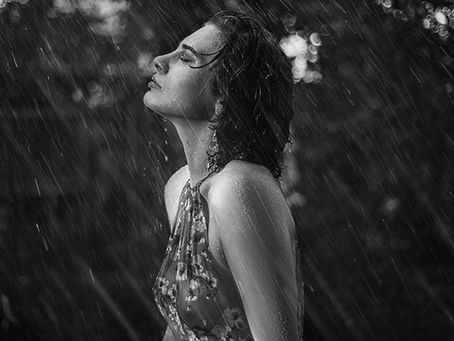 Woman standing in the rain, paying attention to the physical sensation of raindrops on her face as an example of mindfulness and body awareness.