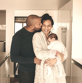 mom holding newborn while being hugged from her partner in the kitchen