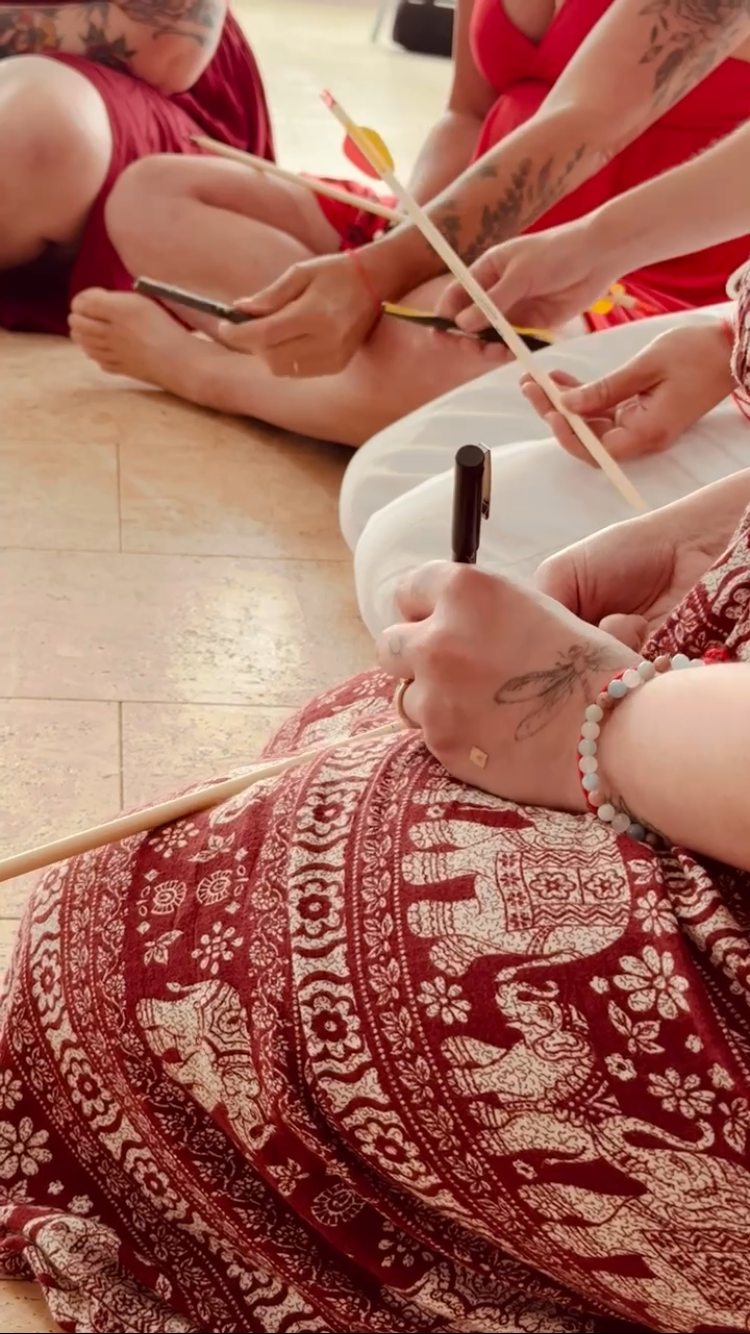 Flower sitting in circle writing her vow to self on her arrow she will break during Goddess Reclaimed Pilgrimage by Amanda Ring in 2024.          Photograph by: Meg Craig