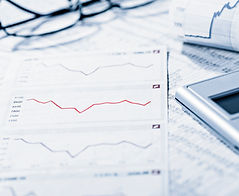 The image shows financial documents featuring charts and graphs, including a red line graph, alongside a calculator and a pair of eyeglasses. A rolled-up report with additional financial data is visible in the background. This image reflects Merlini Group SA's expertise in financing, highlighting their analytical approach and precision in managing financial aspects of real estate projects.