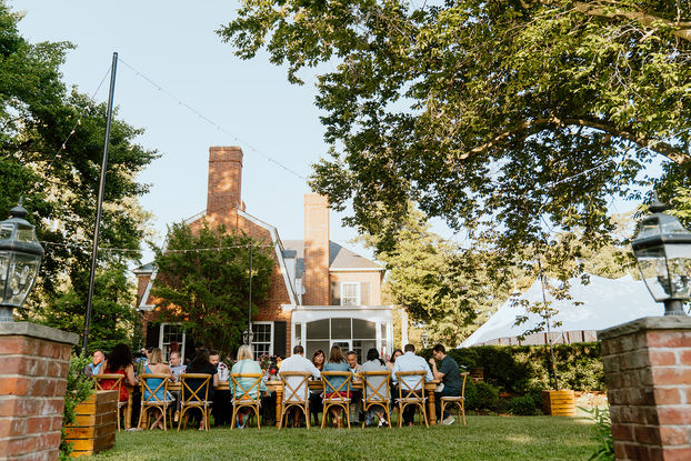 Guests dining at tables on lawn with Brittland Manor in the background at wedding welcome party