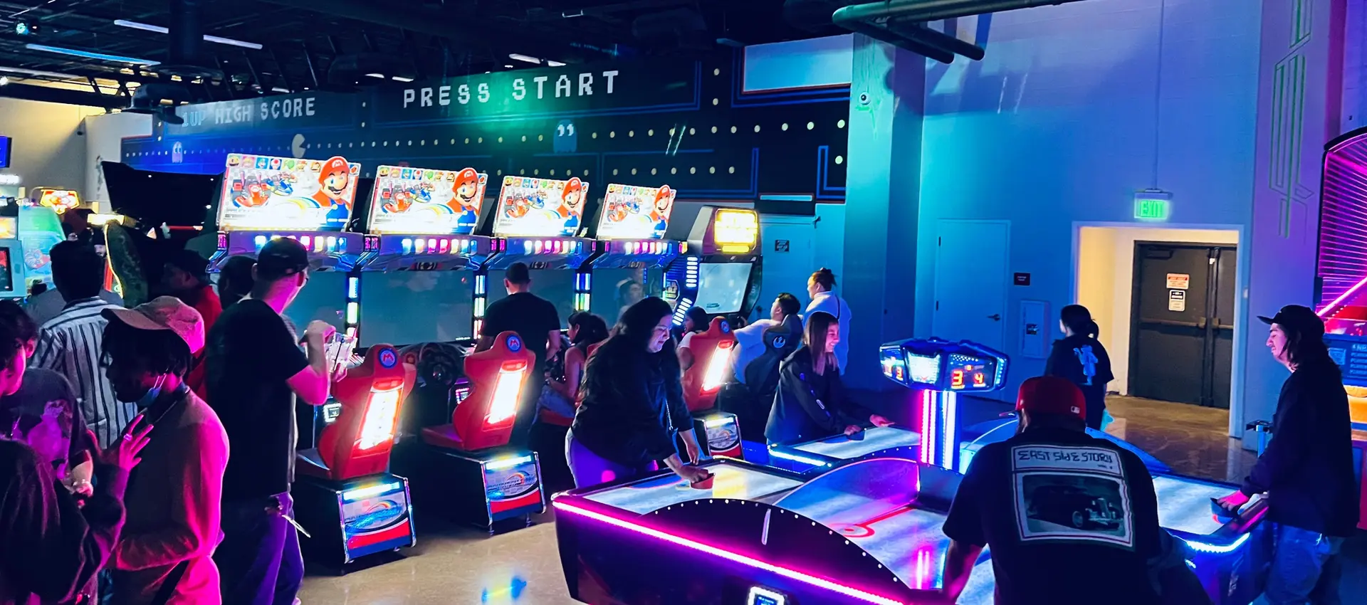 a well lit arcade bar with people playing ski ball and racing games