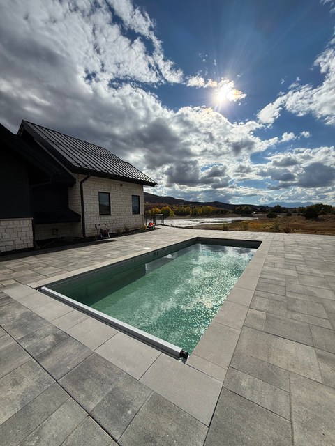 Outdoor pool with blue water and house, cloudy sky, Dirigo Pools