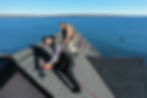 Solar installers secured with safety harnesses working on a steep rooftop overlooking the ocean