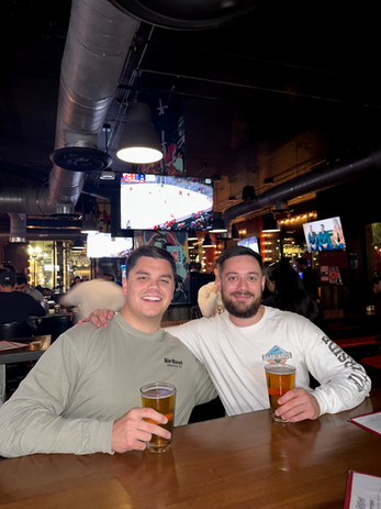 Two men smiling with beers in a bar