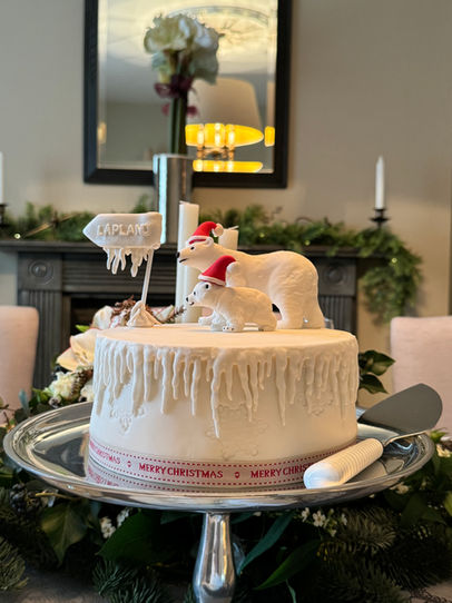 White Christmas Cake with a Polar Bear mother and cub  wearing Santa hats, journeying across wintery landscape to LapLand by Cakes by Rebecca Chipping Campden