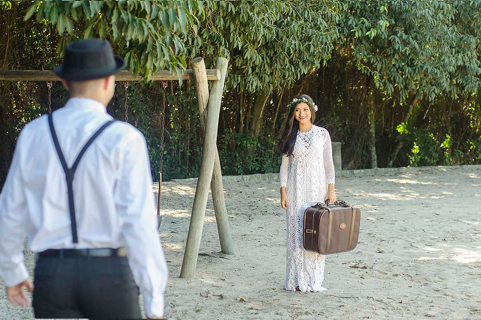 casal se encontrando no bosque, ela segurando uma mala de couro na mão, coroa de flores na cabeça e ele com chapéu do panamá