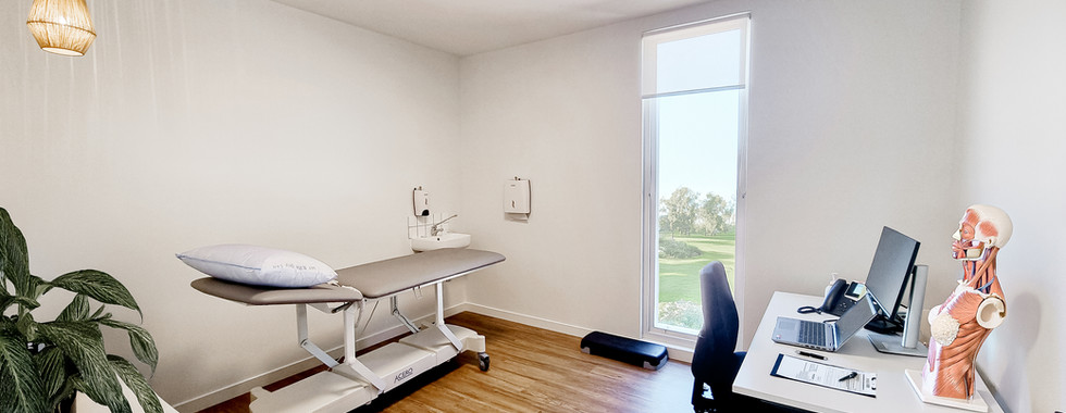 Landscape image of entire consulting suite with therapy bed, desk, computer set up as well as ergonomic chair