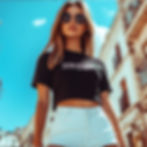 Model rocking the crop top with high-waisted shorts and aviator shades under a blue sky.