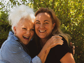 Smiling older woman and her adult daughter hugging outdoors, planning her move into aged care together