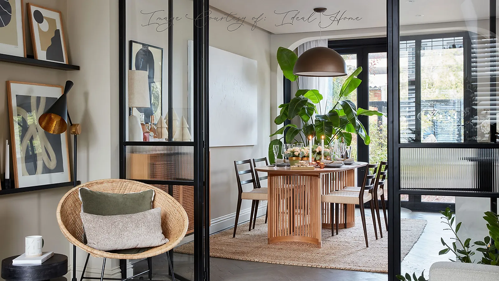 Modern dining area with a wooden table, black chairs, and lit candles. Large plant decorates the space. Neutral tones, abstract art on walls.
