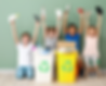 Four diverse children smiling and holding up recyclable items above recycling bins, promoting youth participation in environmental awareness and waste reduction.