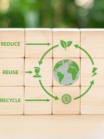 Wooden blocks arranged with green arrows around the Earth, labeled reduce, reuse, recycle.