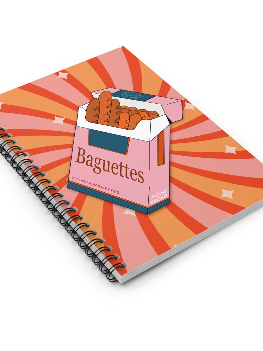 Closed notebook angled on surface, displaying a baguette-themed satirical food cover in pink and orange