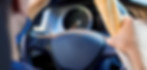 Close-up of someone driving a car with one hand on the wheel and the other holding a baguette like a snack-on-the-go.