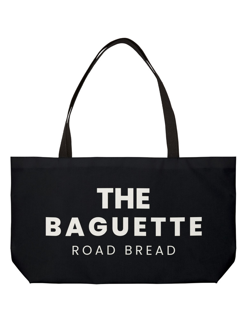Front view of large black canvas tote bag with white block text reading “THE BAGUETTE ROAD BREAD”