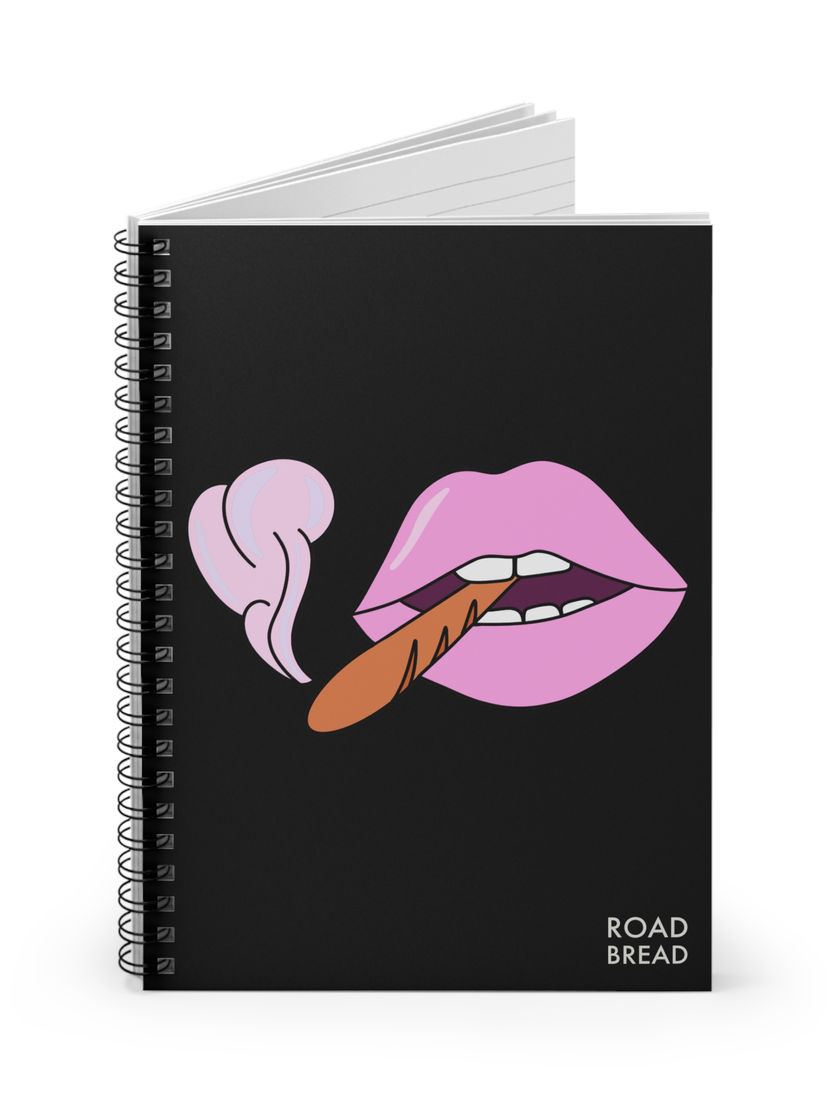 Black spiral notebook with a pink pop art lips graphic puffing a baguette, bold "ROAD BREAD" logo in bottom corner