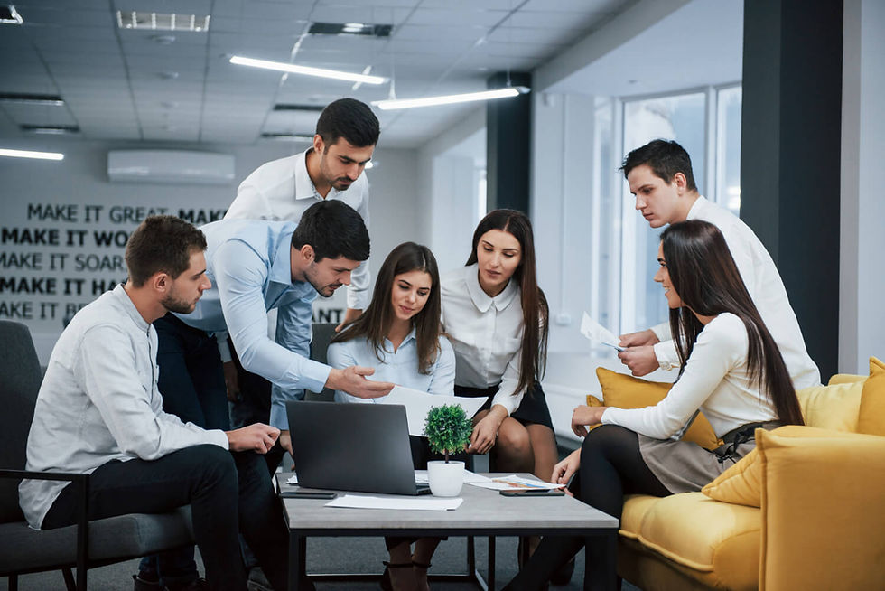 reunião empresarial com três mulheres e quatro homens todos vestidos socialmente sentados em um sofá envolta de uma mesa de centro