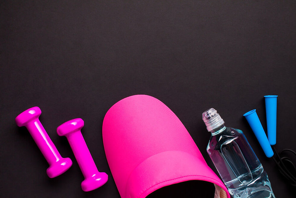 A imagem mostra um conjunto de itens de academia dispostos sobre um fundo preto. À esquerda, há dois halteres pequenos de cor rosa brilhante. No centro, aparece um boné rosa vibrante, parcialmente visível. À direita, há uma garrafa de água transparente e, ao lado dela, dois bicos ou cones de silicone azul, provavelmente acessórios de treino ou de hidratação. O arranjo tem um visual colorido, moderno e voltado para atividades fitness ou esportivas.