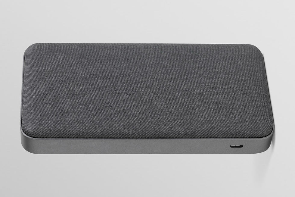 A imagem mostra um HD externo em pé, com design moderno e minimalista. Ele possui cantos arredondados e é revestido por um material têxtil escuro (cinza grafite), que dá um aspecto elegante e sofisticado. Na lateral, é visível uma entrada USB-C para conexão. O corpo do dispositivo tem acabamento metálico fosco, transmitindo robustez e durabilidade. O estilo clean e discreto sugere que é um produto voltado para quem busca praticidade e estética ao mesmo tempo.
