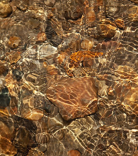 Image of the nearby River with glassy ripples over rocks of various shades of brown.